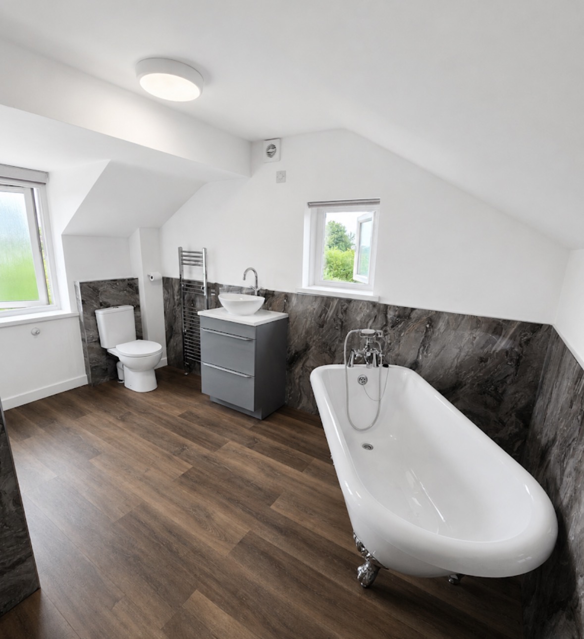 Loft bathroom with freestanding slipper bath, grey marble panelling and wood-effect flooring