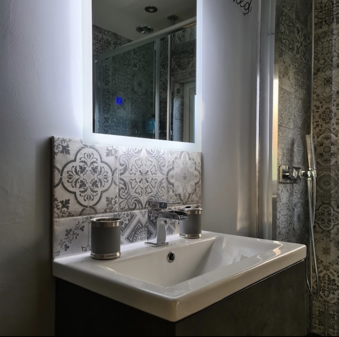 Patterned tiled bathroom with illuminated mirror and wall-hung vanity unit