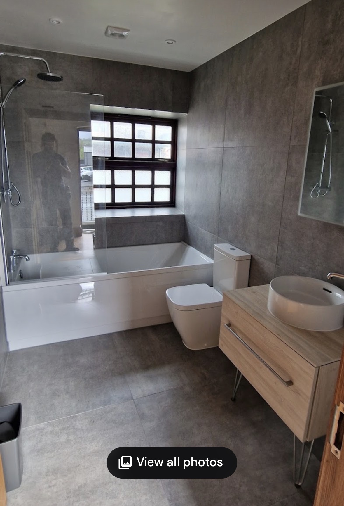 Grey large-format tiled bathroom with bath, shower screen and oak vanity unit