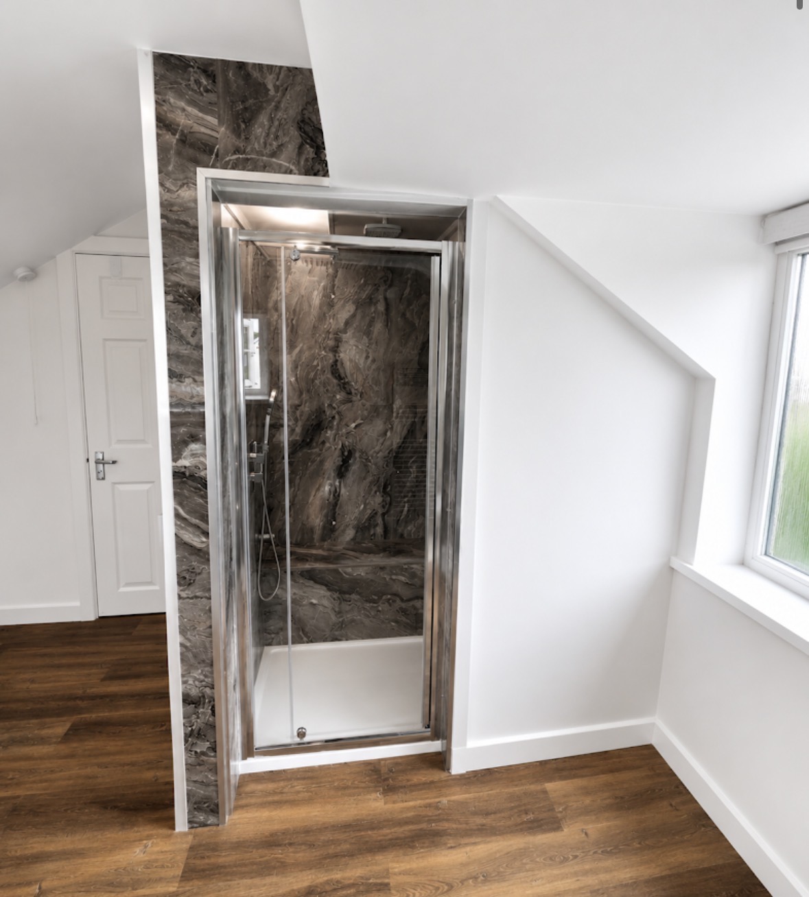 Marble-panelled shower enclosure fitted into a sloped loft space